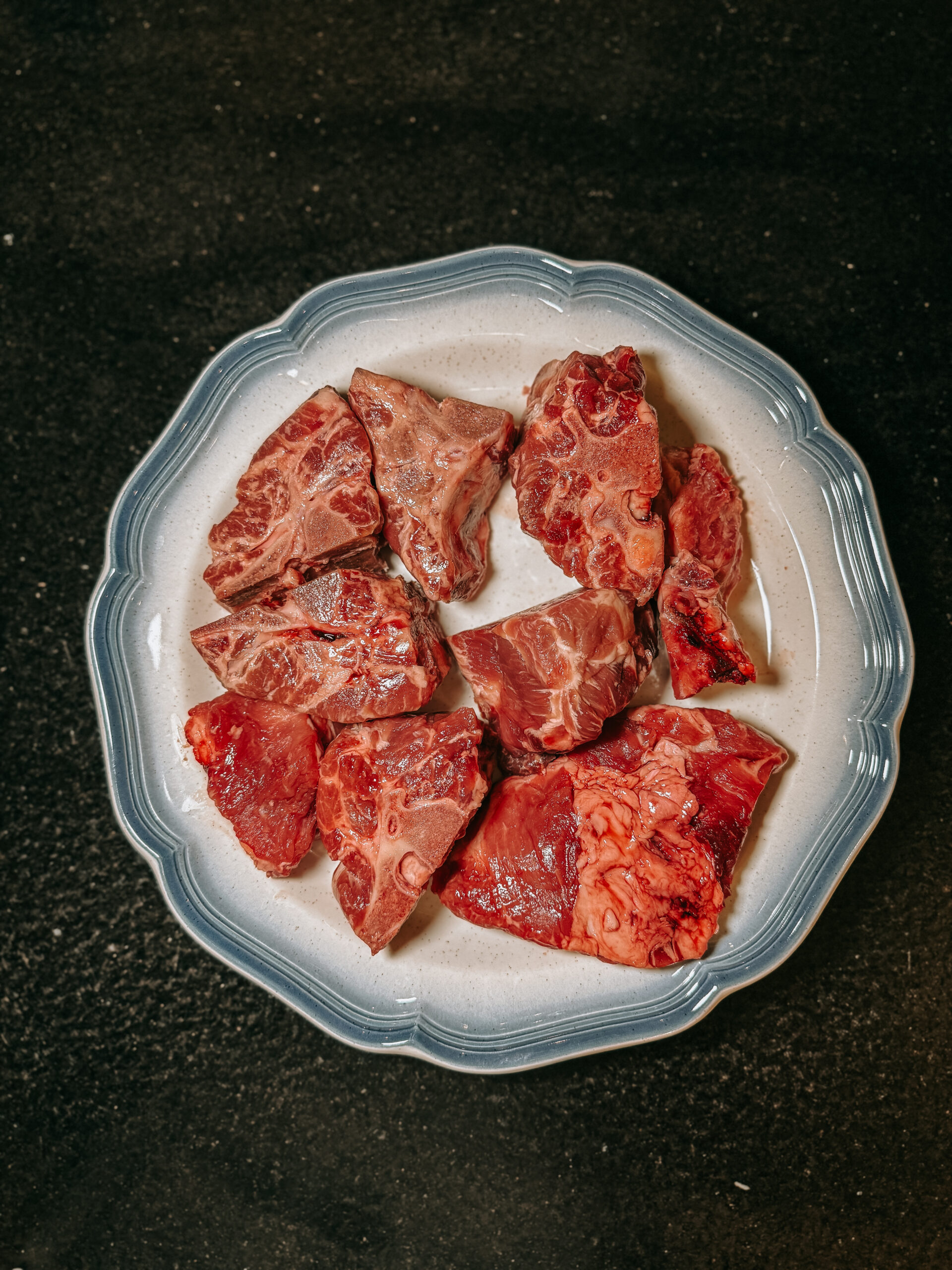 Assorted raw meat cuts arranged on a decorative plate, showcasing various textures and colors, ideal for cooking or meal preparation.